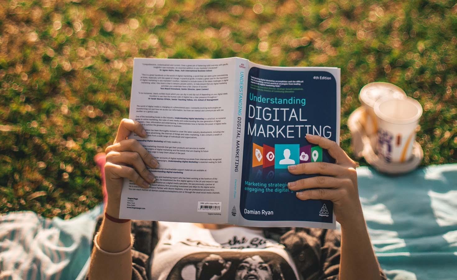 Person reading "Digital Marketing" book outside.