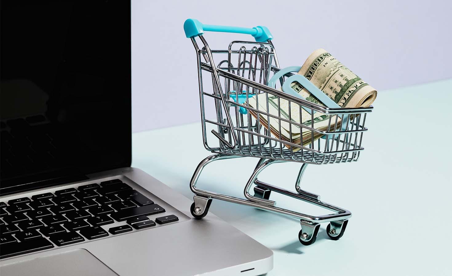 Toy shopping cart with money in it on a laptop computer