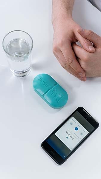Folded hands on a desk next to a phone, glass of water, and a large pill.